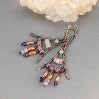 Earrings with white and purple stones wired to a triangular copper frame
