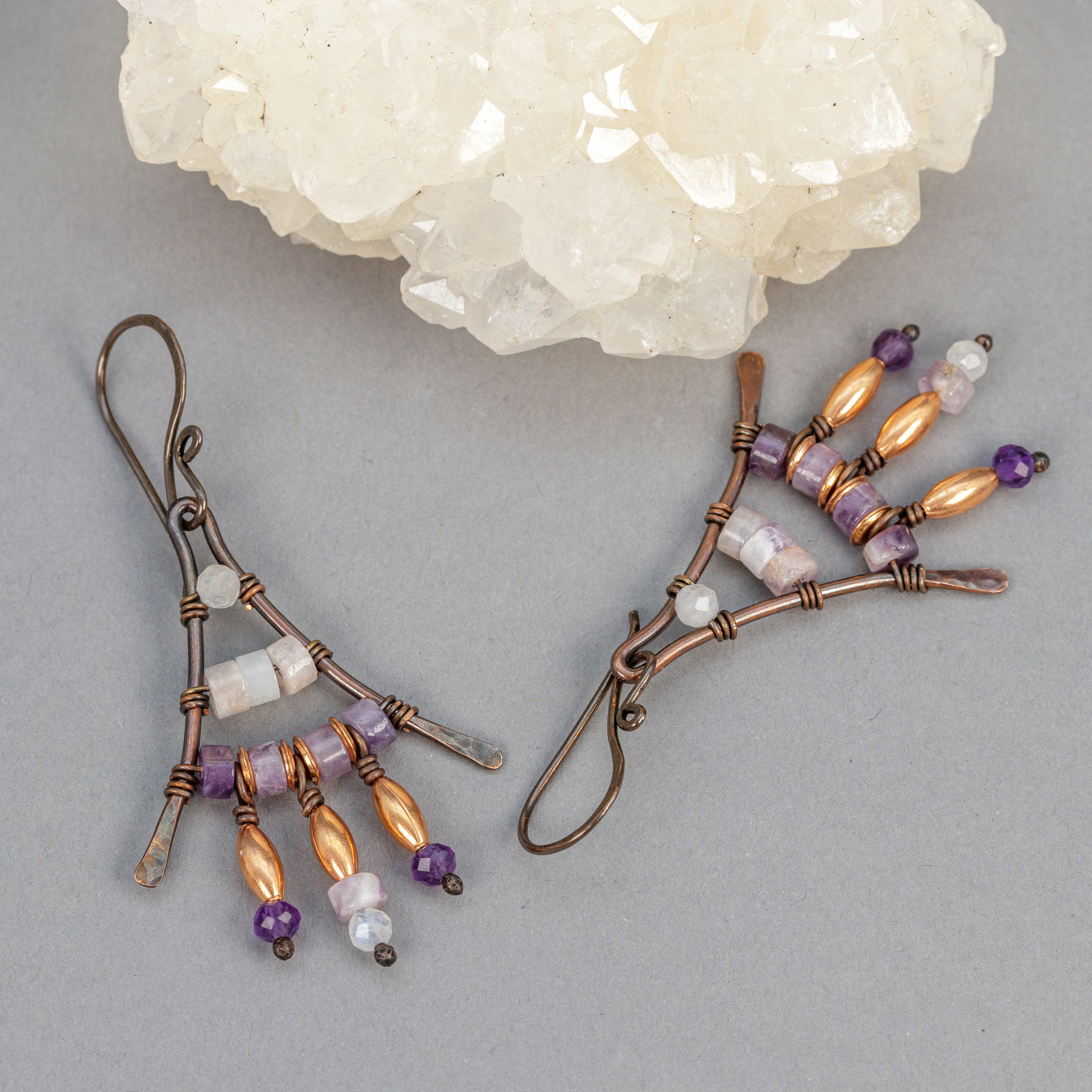 Earrings with white and purple stones wired to a triangular copper frame
